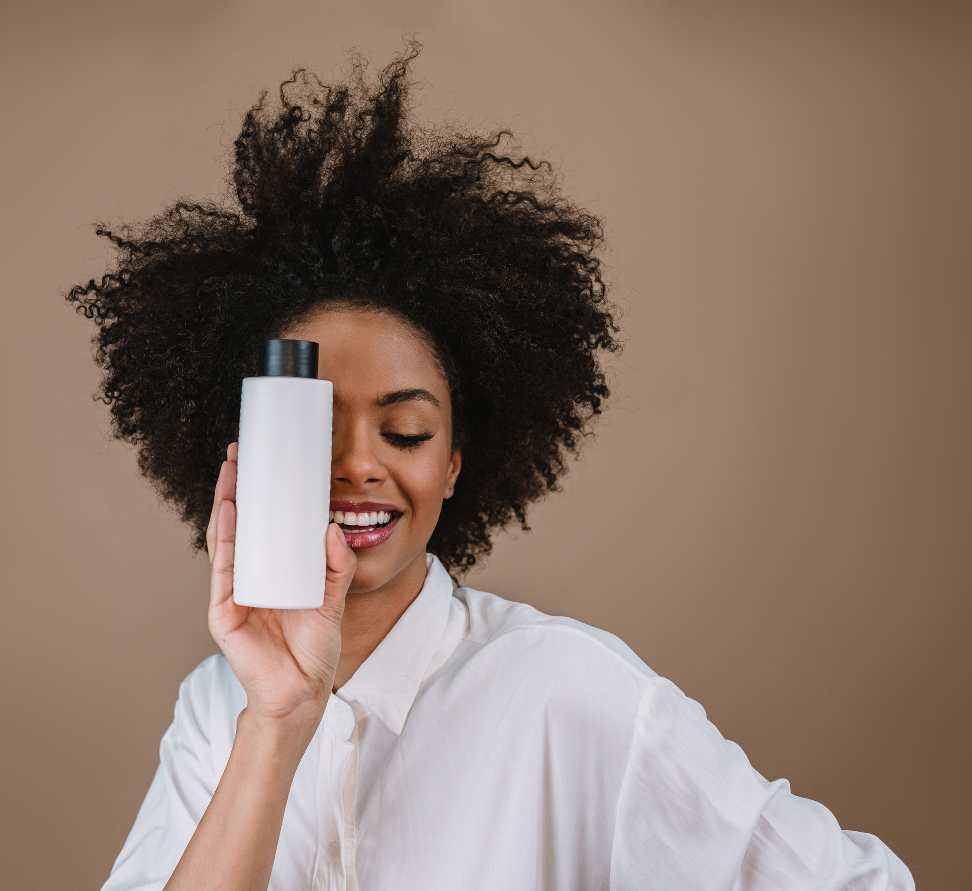 Beauty Latin woman with afro hairstyle. Brazilian woman. Holding blank shampoo packaging. Curly hair. Hair style. Pastel background.